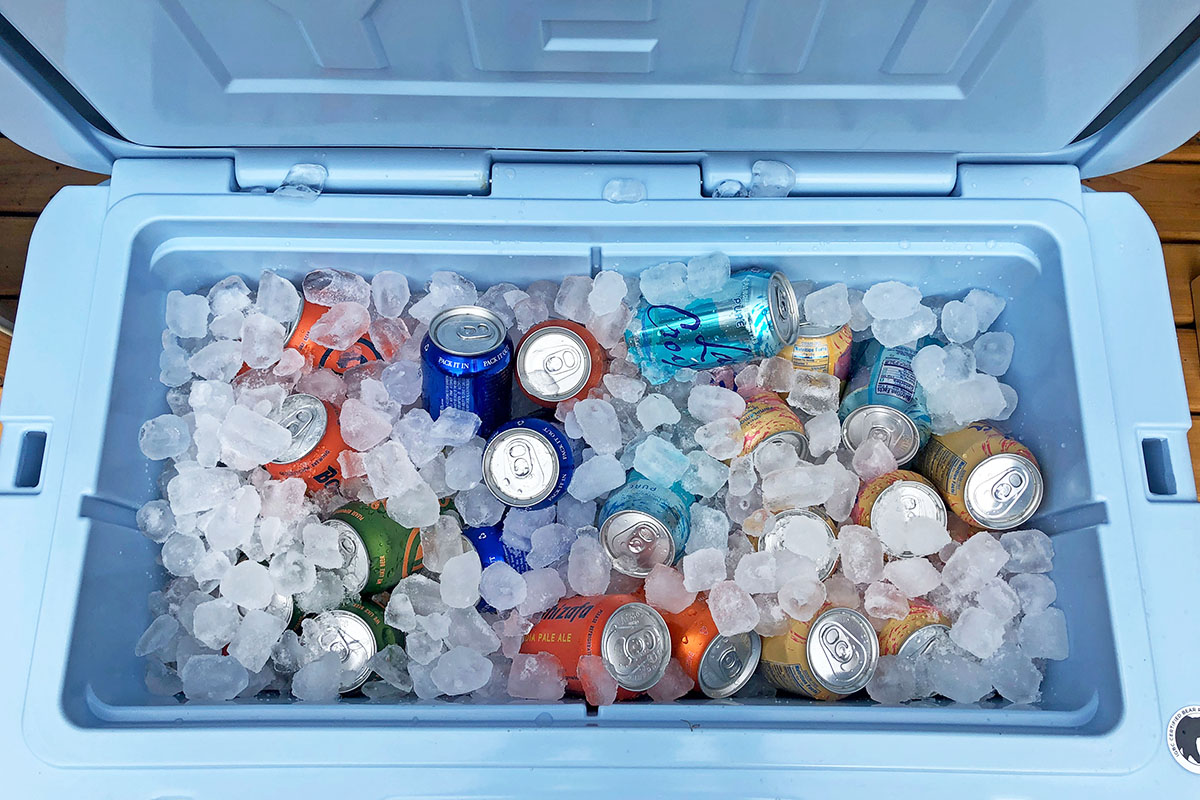A cooler is packed to the top with crushed ice and cold cans.